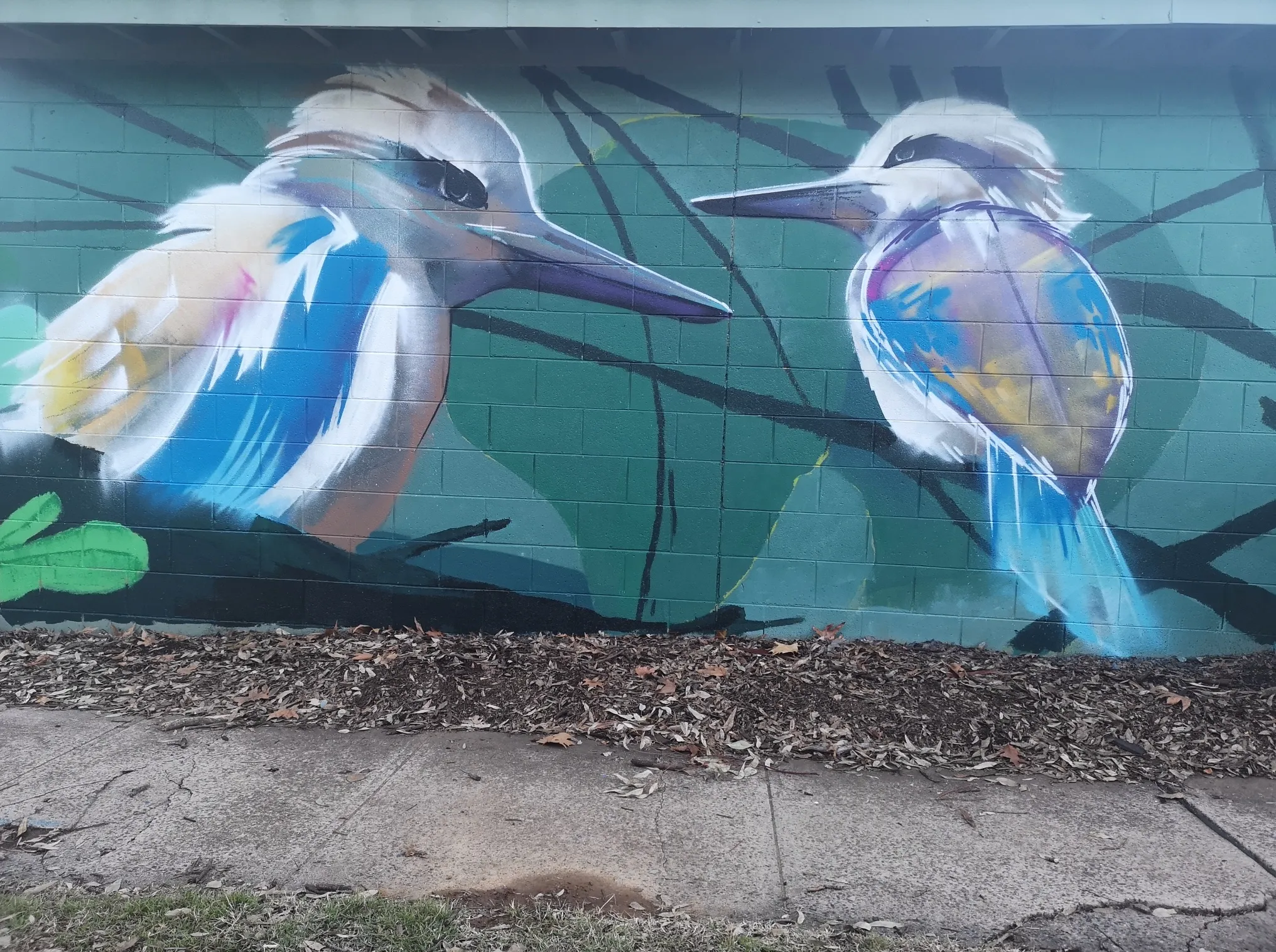 Mural of two sacred kingfisher birds among red flowers, painted on a besser-block wall