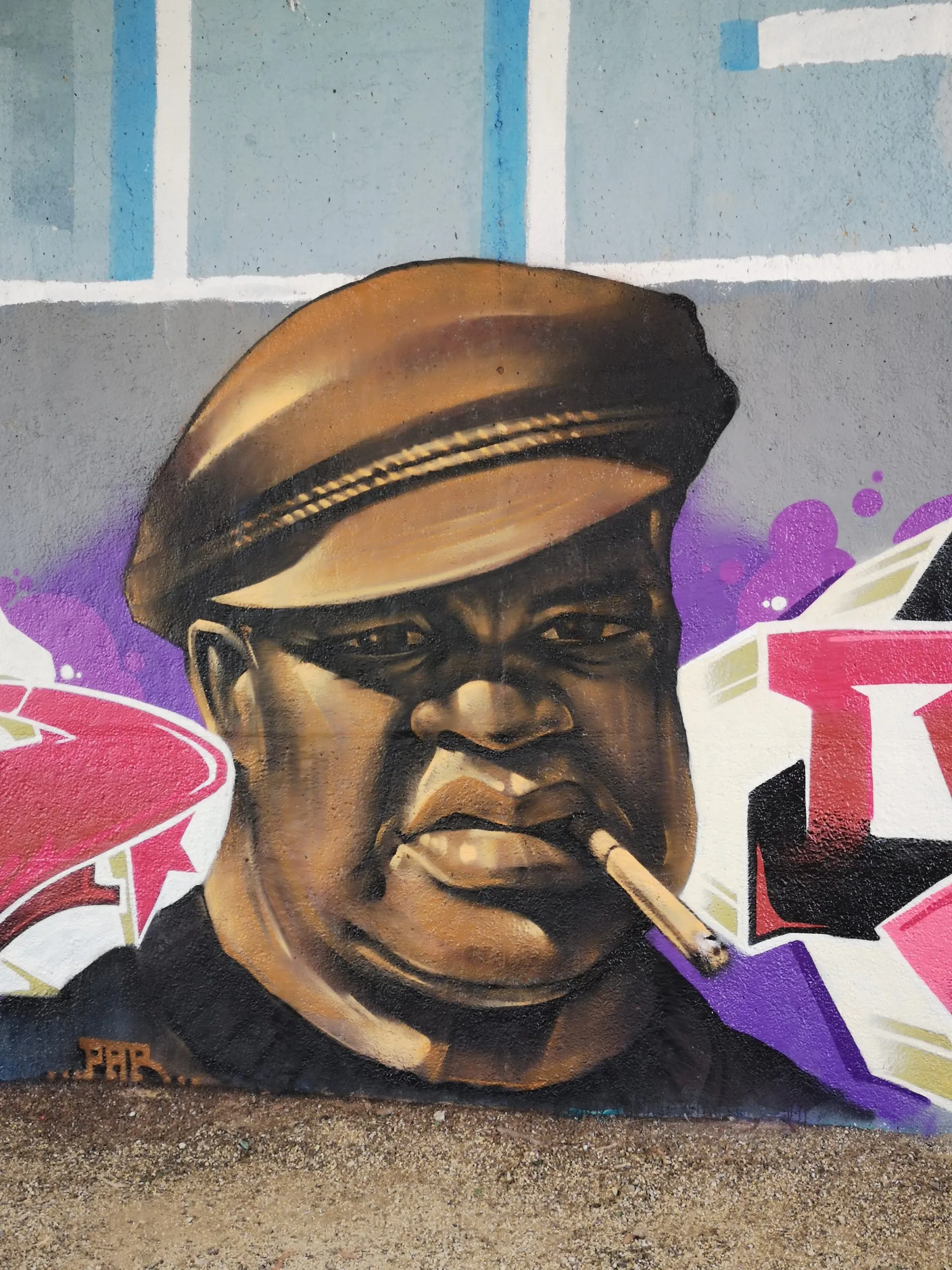 Portrait mural of a man in a flat cap smoking, painted in a realist style against a grey and blue wall