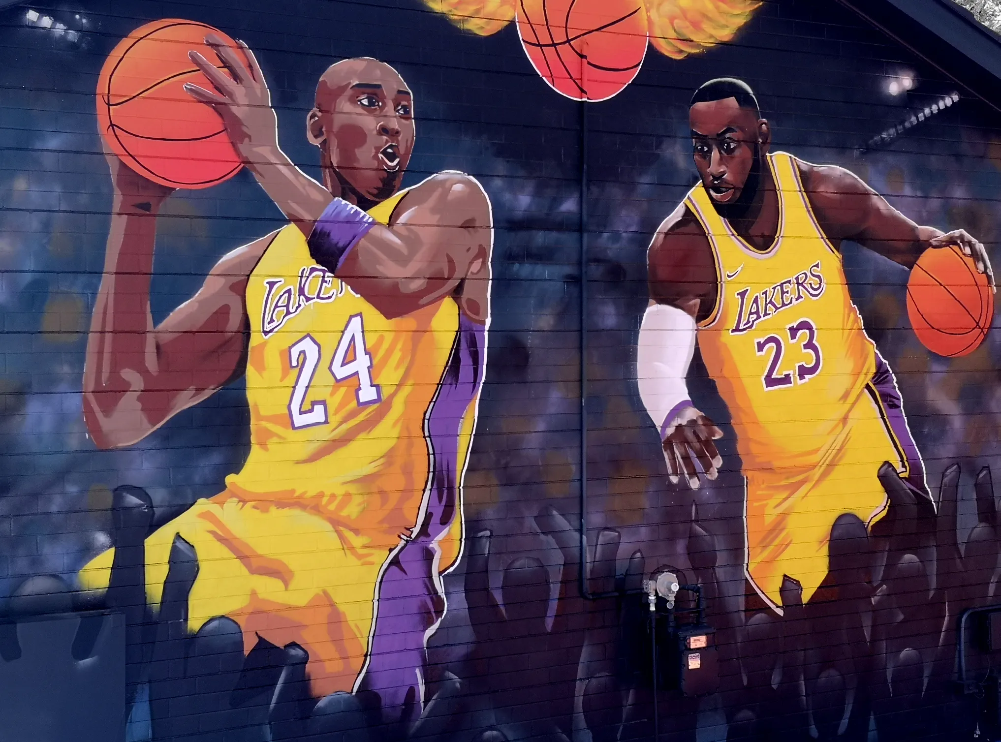Mural of two basketball players in Lakers jerseys mid-game, painted on a dark wall