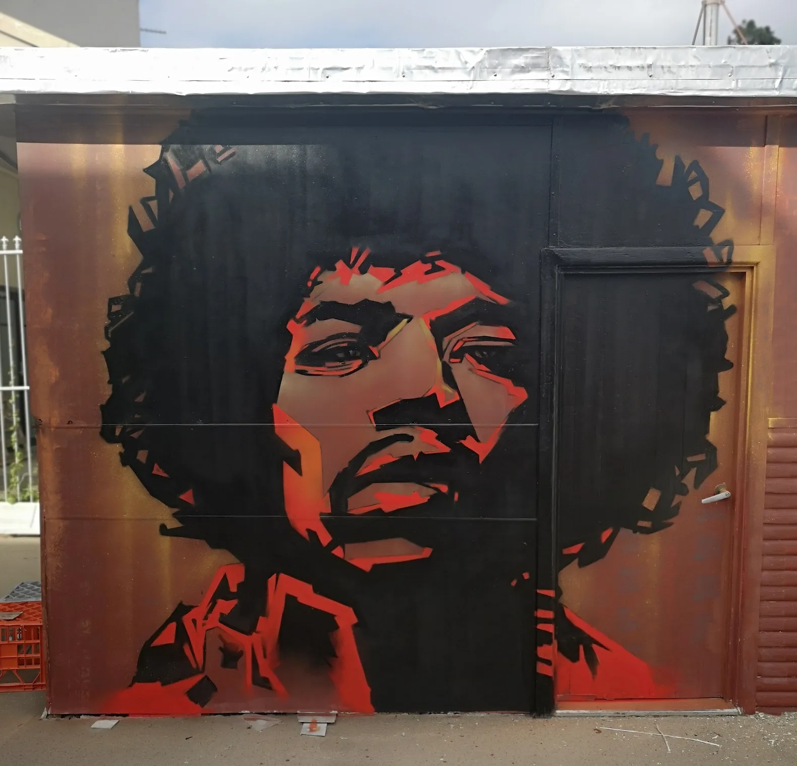 Stencil-style portrait mural of a musician with an afro, in black and red on a gold wall