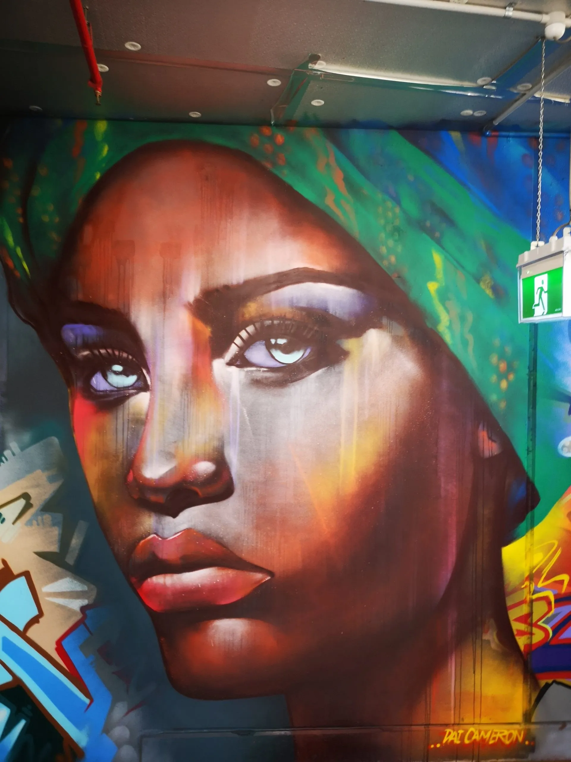 Large portrait mural of a woman in a green headscarf, painted in bold colour