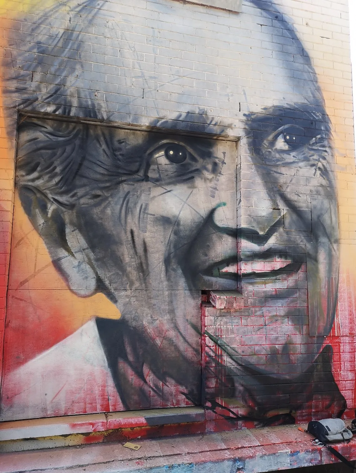 Portrait mural of a smiling elderly man in greys against warm red and orange