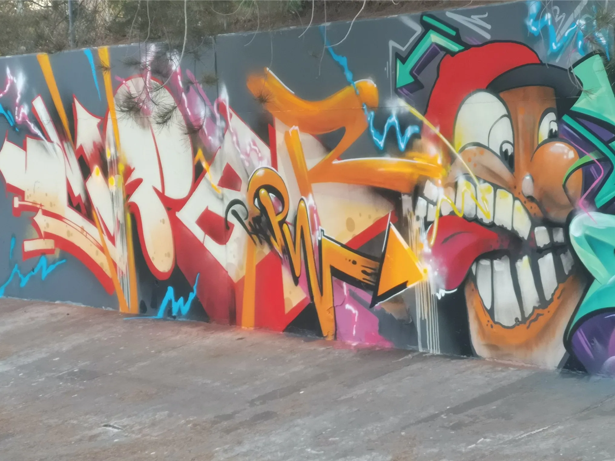 Graffiti wall with colourful wildstyle lettering and a grinning cartoon character