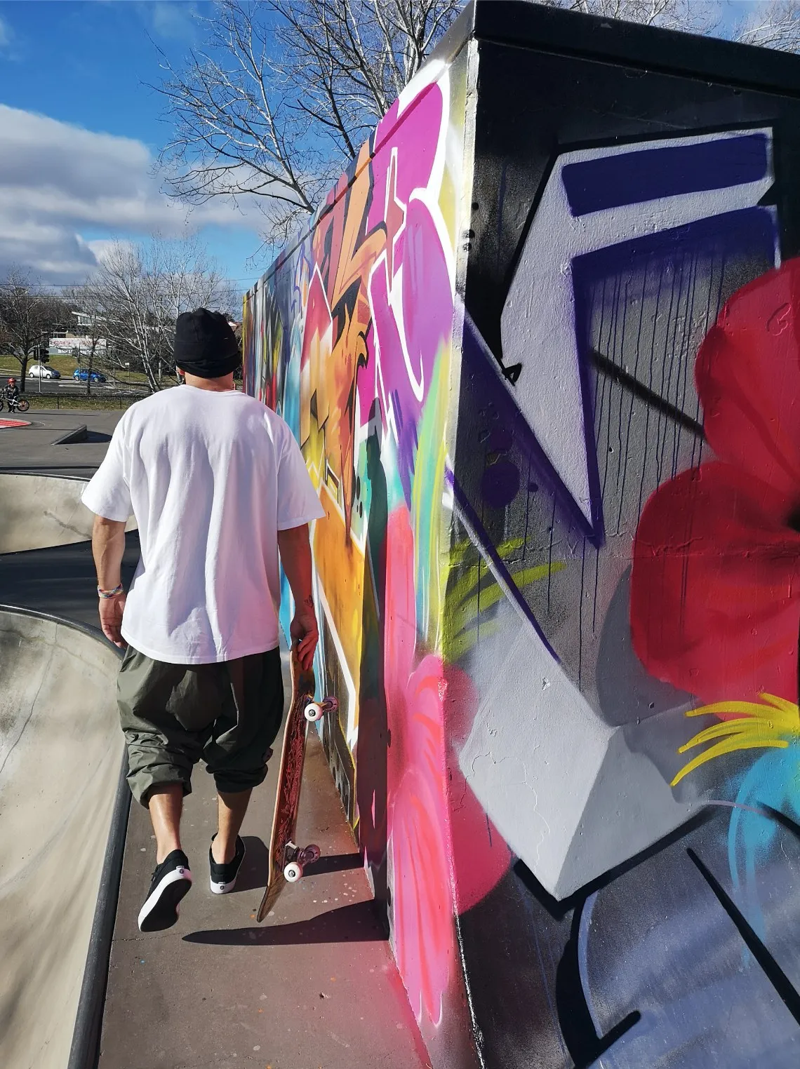 Person walking past a long graffiti wall painted in bright pinks, purples and blues