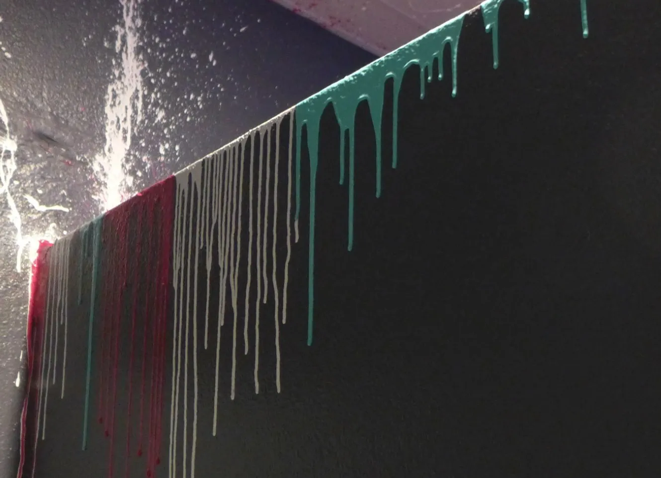 Long black wall with white and green paint drips running down from the top