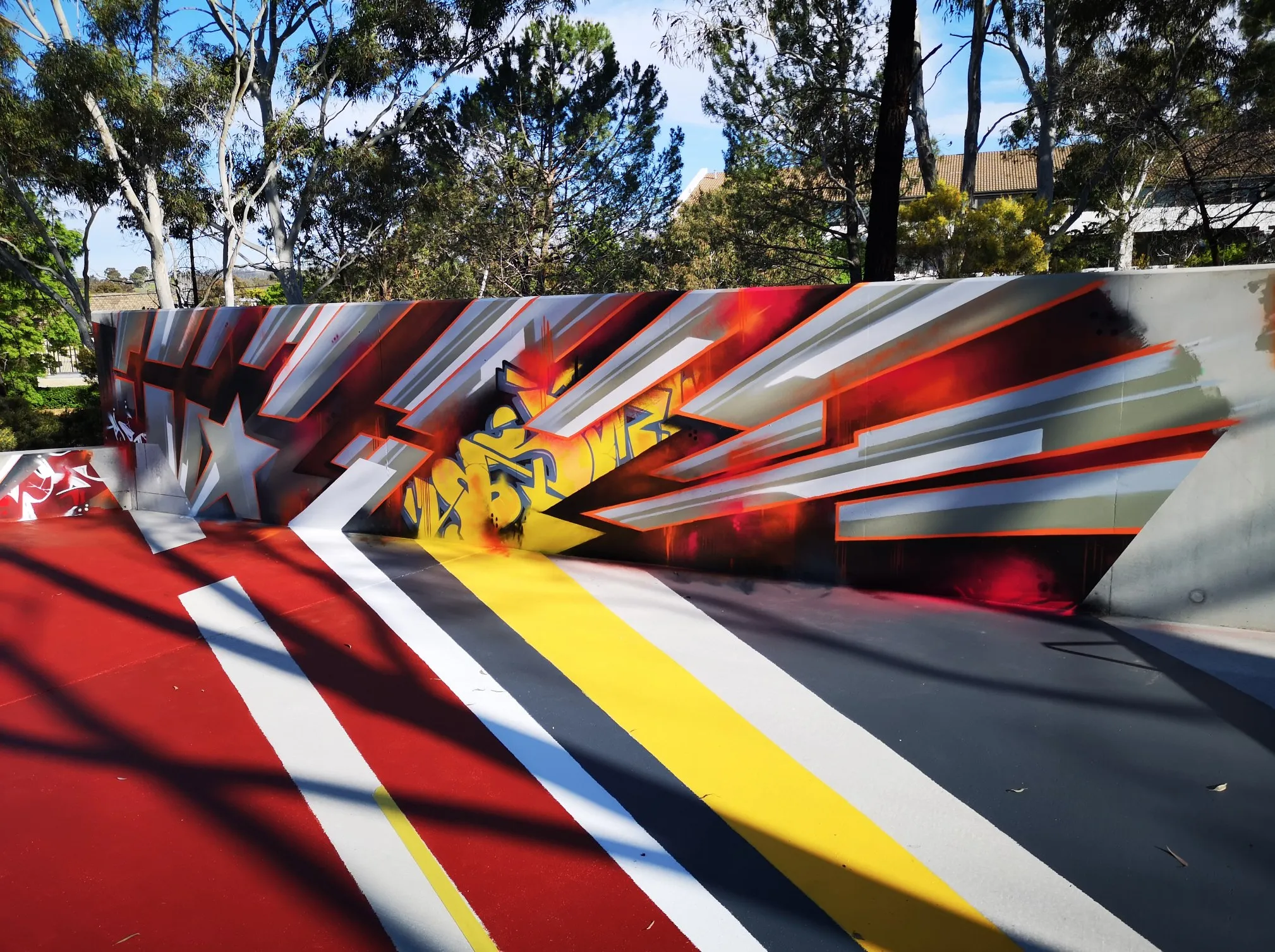 Geometric mural of red, white, grey and yellow stripes across a curved concrete wall in a park